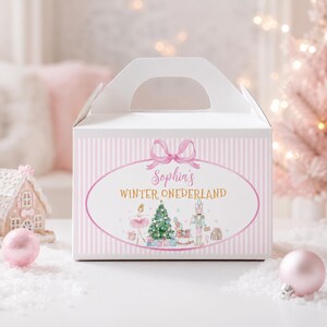May include: A white gable box with a light pink striped pattern. The front features an oval frame with a pink bow, the text "Sophia's WINTER ONEDERLAND," and illustrations of a ballerina, a Christmas tree, a rocking horse, and a nutcracker.