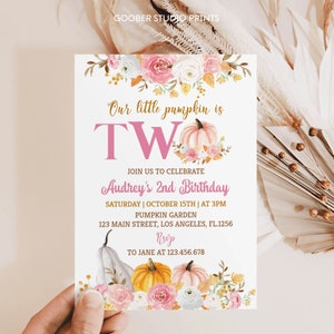 May include: A white invitation card featuring floral and pumpkin illustrations. The text reads "Our little pumpkin is TWO" in pink and gold. Details include the birthday girl's name, date, time, location, and RSVP information. The card is decorated with watercolor pumpkins and flowers.