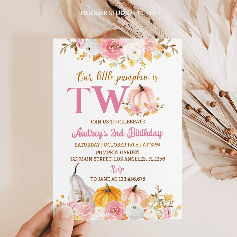 May include: A white invitation card featuring floral and pumpkin illustrations. The text reads "Our little pumpkin is TWO" in pink and gold. Details include the birthday girl's name, date, time, location, and RSVP information. The card is decorated with watercolor pumpkins and flowers.