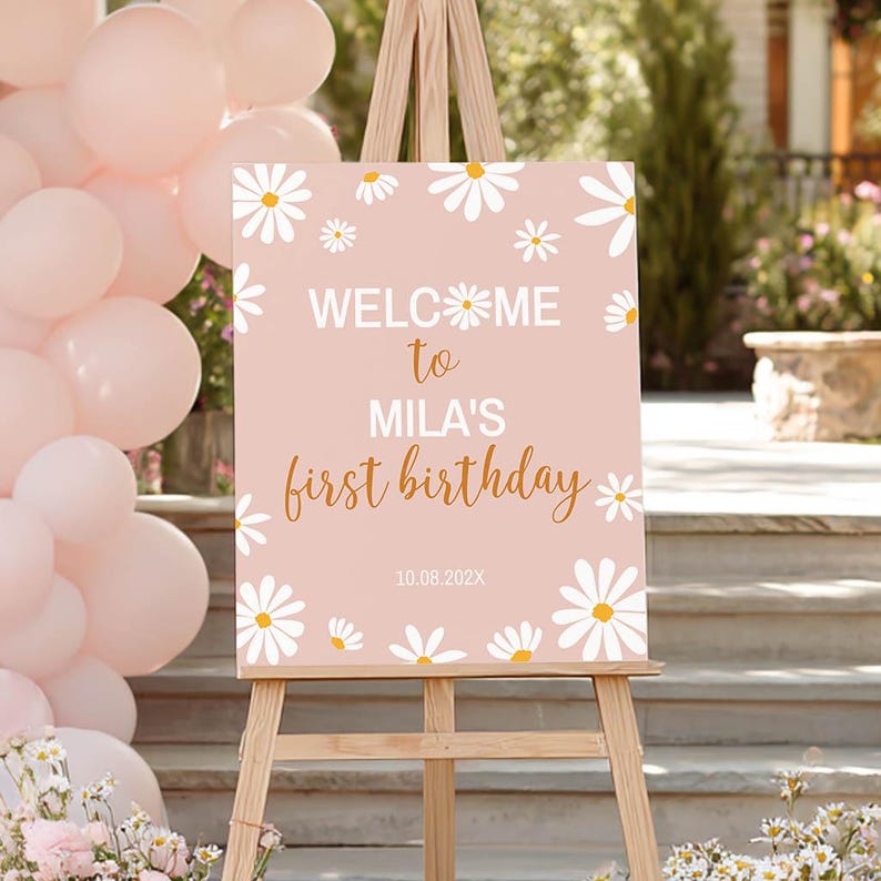 Op de afbeelding: Een rechthoekig bord op een houten ezel met een lichtroze achtergrond en witte madeliefjesillustraties. De tekst luidt: WELCOME to MILA'S first birthday 10.08.202X. WELCOME is wit, to is goud, MILA'S is wit en first birthday is goud.