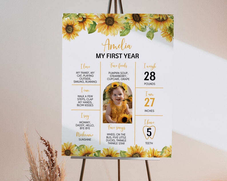 May include: A white poster with a sunflower border and a photo of a baby girl. The poster is titled "Amelia My First Year" and includes information about the baby's age, weight, height, favorite foods, songs, and a tooth.