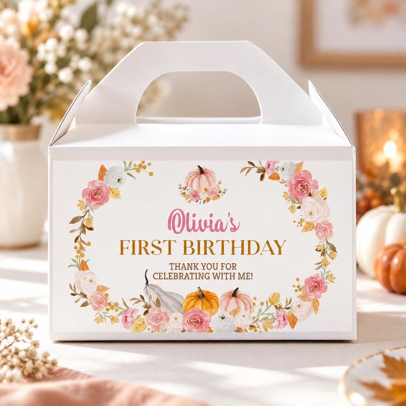 May include: A white cardboard gable box featuring a floral wreath design with pink and white flowers, orange and white pumpkins, and the text "Olivia's FIRST BIRTHDAY THANK YOU FOR CELEBRATING WITH ME!" printed in pink and gold on the front panel.