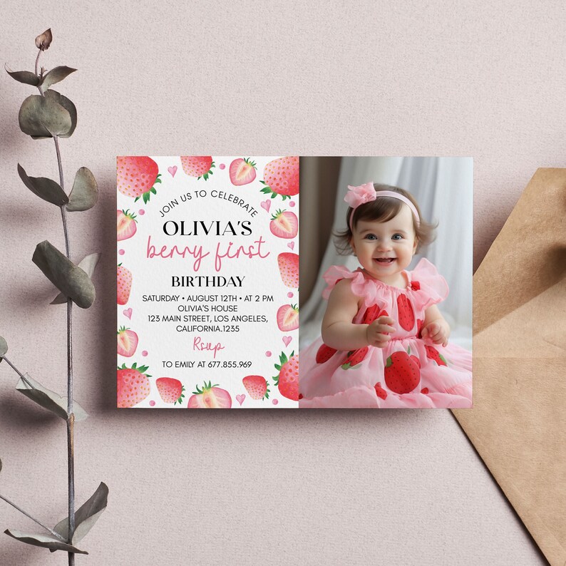 May include: A rectangular birthday invitation card featuring a white background with watercolor strawberry illustrations and pink hearts. The text reads: JOIN US TO CELEBRATE OLIVIA'S berry first BIRTHDAY, SATURDAY AUGUST 12TH AT 2 PM, OLIVIA'S HOUSE, 123 MAIN STREET, LOS ANGELES, CALIFORNIA.1235, RSVP, TO EMILY AT 677.855.969. A photo of a smiling child in a strawberry-patterned dress is on the right.