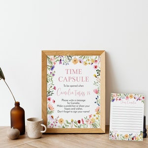 May include: A framed sign and a matching card featuring watercolor wildflowers. The sign reads: TIME CAPSULE To be opened when Camelia Turns 18. Please write a message for Camelia. Make a prediction or share your hopes and wishes. Don't forget to sign your name!