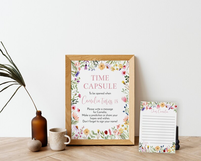 May include: A framed sign and a matching card featuring watercolor wildflowers. The sign reads: TIME CAPSULE To be opened when Camelia Turns 18. Please write a message for Camelia. Make a prediction or share your hopes and wishes. Don't forget to sign your name!