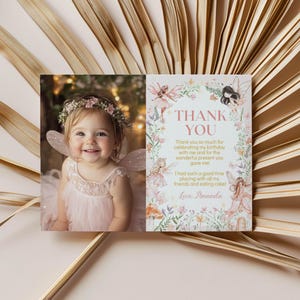 May include: A pink thank you card with a photo of a young girl wearing a fairy costume and a flower crown. The card has a floral border and the text "Thank You" in pink. The text reads "Thank you so much for celebrating my birthday with me and for the wonderful present you gave me! I had such a good time playing with all my friends and eating cake! Love, Amanda."