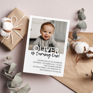 Op de afbeelding: Een rechthoekige verjaardagsuitnodiging met een foto van een baby, met de tekst OLIVER is turning One! gevolgd door evenementdetails zoals zaterdag 12 oktober om 14:00 uur, The Flower Garden, 123 Main Street, Los Angeles, CA.