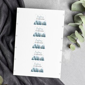 May include: A white rectangular sheet featuring five identical labels arranged vertically. Each label displays the text Easton's 1ST BIRTHDAY above a watercolor illustration of a blue-toned pine forest with a small deer and snowflakes.