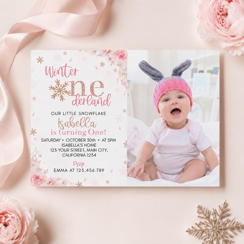 May include: A rectangular birthday invitation card featuring pink floral accents, gold snowflake graphics, and the text Winter onederland. The card includes details for Isabella turning one, with a photo of a baby wearing a pink knit hat with ears.