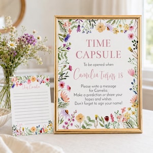 May include: A gold-framed sign and a matching card featuring watercolor wildflowers. The sign reads: TIME CAPSULE To be opened when Camelia Turns 18. Please write a message for Camelia. Make a prediction or share your hopes and wishes. Don't forget to sign your name!