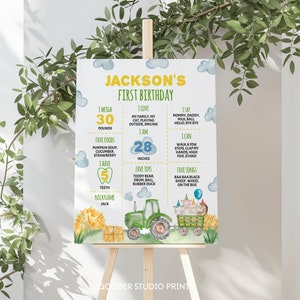 May include: A rectangular birthday milestone sign for Jackson's first birthday featuring watercolor illustrations of a green tractor, hay bales, and farm animals. The white sign includes yellow and green text detailing weight, height, and favorite things.