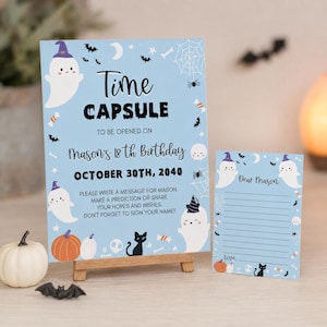 May include: A light blue time capsule sign and matching card featuring ghosts, pumpkins, black cats, and bats. The sign reads: Time CAPSULE TO BE OPENED ON Mason's 18th Birthday OCTOBER 30TH, 2040. PLEASE WRITE A MESSAGE FOR MASON.