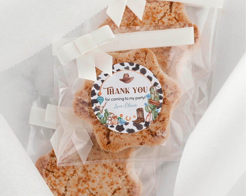 May include: Star-shaped cookies in clear plastic bags tied with white ribbons. Each bag features a round sticker with a cow print border, a brown cowboy hat, a boot, cacti, and the text: THANK YOU for coming to my party! Love, Oliver.