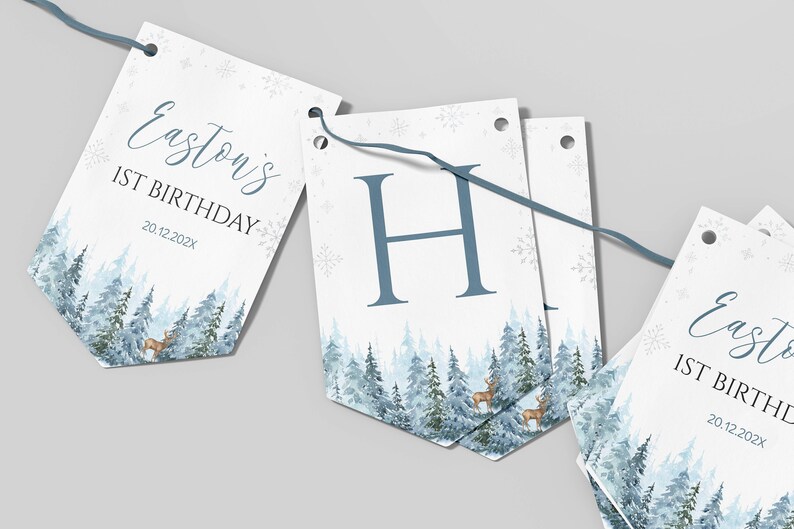 Puede incluir: Una guirnalda decorativa de papel con tem&aacute;tica de bosque invernal, pinos azules, ciervos y copos de nieve. Los banderines muestran el texto Easton's 1ST BIRTHDAY 20.12.202X y la letra H, unidos por un cord&oacute;n azul para colgar.