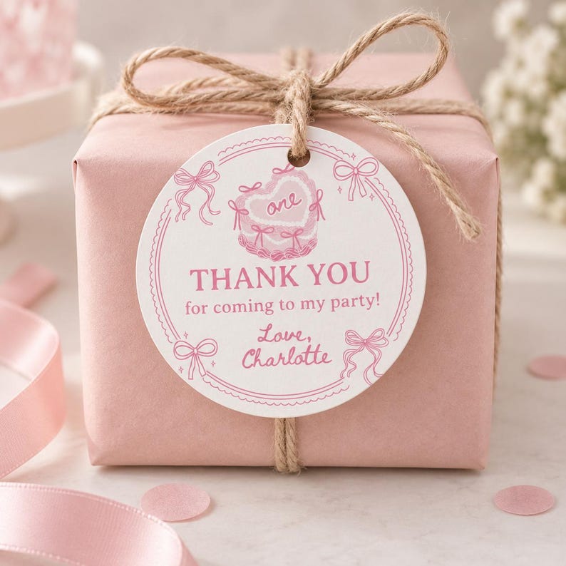 K&ouml;nnte beinhalten: Eine quadratische Geschenkbox in einfarbigem rosa Papier, gebunden mit nat&uuml;rlicher brauner Schnur. Ein rundes wei&szlig;es Etikett ist befestigt, mit rosa Illustrationen von Schleifen und einer herzf&ouml;rmigen Torte mit dem Text: one, THANK YOU for coming to my party!, Love, Charlotte.
