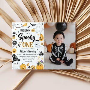 May include: A Halloween-themed invitation with the text "Jackson is a Spooky ONE" and a photo of a baby in a skeleton costume. The invitation features illustrations of ghosts, pumpkins, bats, and candy. The baby is wearing a black beanie.