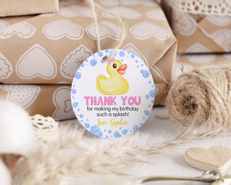 Pu&ograve; includere: Un'etichetta regalo rotonda bianca con una papera di gomma gialla con un fiocco rosa, bolle blu e il testo THANK YOU for making my birthday such a splash! Love Sophia. L'etichetta &egrave; sospesa da un sottile spago di juta per i regali.