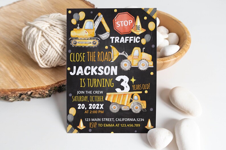May include: A rectangular birthday invitation card with a black chalkboard background featuring yellow construction vehicles, orange traffic cones, and balloons. The text reads: STOP THE TRAFFIC, CLOSE THE ROAD, JACKSON IS TURNING 3 YEARS OLD!