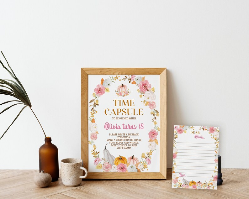 K&ouml;nnte beinhalten: Ein gerahmtes Schild mit einem Blumen- und K&uuml;rbiskranz um den Text TIME CAPSULE TO BE OPENED WHEN Olivia turns 18 sowie Anweisungen. Daneben liegt eine passende linierte Karte mit dem Text DEAR Olivia und Love.