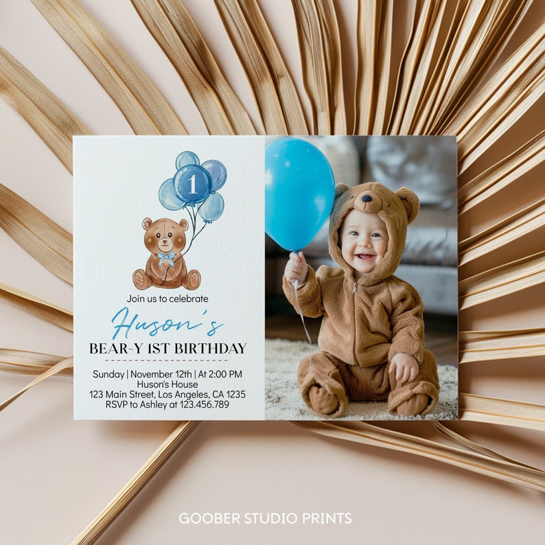 Op de afbeelding: Een rechthoekige verjaardagsuitnodigingskaart met een aquarelillustratie van een bruine teddybeer die blauwe ballonnen met het cijfer &eacute;&eacute;n vasthoudt. De tekst luidt Huson's BEAR-Y 1ST BIRTHDAY, zondag 12 november om 14:00 uur, 123 Main Street, Los Angeles, CA 1235, RSVP aan Ashley op 123.456.789. Een foto van een kind in een berenkostuum met een blauwe ballon is inbegrepen.