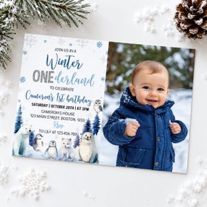 May include: A rectangular birthday invitation card featuring a photo of a child in a navy blue winter jacket on the right. The left side displays text reading Winter ONEderland, Cameron's 1st birthday, and details, with illustrations of a polar bear, penguins, a fox, a seal, and an owl.
