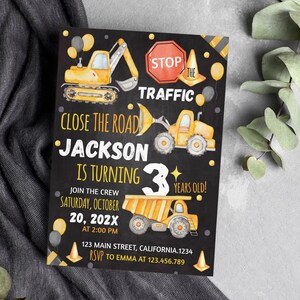 May include: A rectangular invitation card with a black background featuring yellow construction vehicles, orange traffic cones, and black and yellow balloons. The text reads: STOP THE TRAFFIC, CLOSE THE ROAD, JACKSON IS TURNING 3 YEARS OLD.
