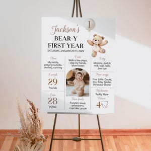 May include: A white poster with a brown teddy bear illustration and the text "Jackson's Bear-Y First Year" with the date "Saturday, January 25th, 202X". The poster also includes information about the child's weight, height, favorite foods, and activities.
