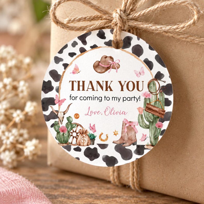 K&ouml;nnte beinhalten: Ein rundes Geschenkanh&auml;nger mit schwarz-wei&szlig;em Kuhfleckenmuster am Rand, verziert mit Aquarellillustrationen von Cowboyhut, Kaktus, Stiefeln und Schmetterlingen. Der Text lautet: THANK YOU for coming to my party! Love, Olivia, in Braun und Rosa.