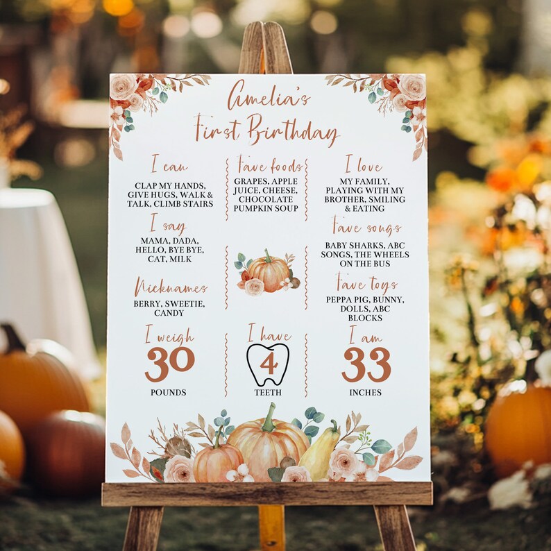 May include: A white rectangular birthday milestone sign featuring copper-colored text and watercolor pumpkin illustrations. The sign lists Amelia's first birthday details including weight of 30 pounds, 4 teeth, and height of 33 inches.