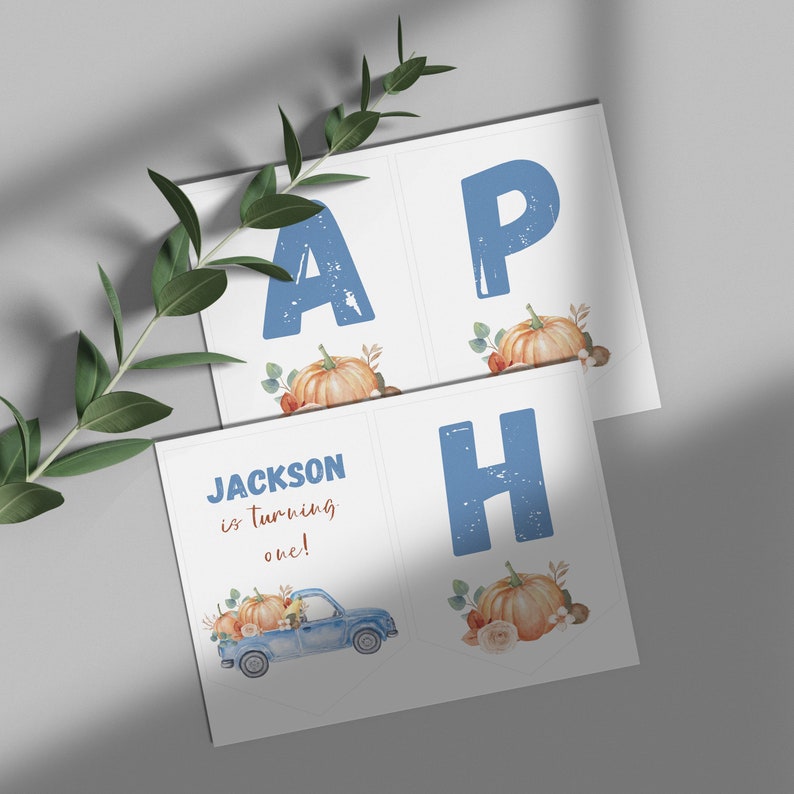 May include: A set of white rectangular banner cards featuring blue distressed letters A, P, and H, alongside watercolor illustrations of orange pumpkins and greenery. One card displays the blue text Jackson is turning one with a blue truck.