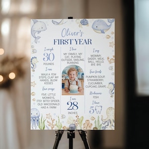 May include: A white milestone poster titled Oliver's First Year featuring blue text and watercolor sea creatures like dolphins, whales, and jellyfish. It includes a central photo of a child, lists personal facts, and measures 28 inches.