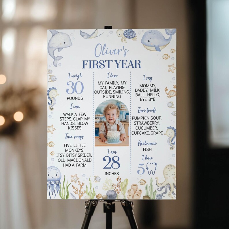 May include: A white milestone poster titled Oliver's First Year featuring blue text and watercolor sea creatures like dolphins, whales, and jellyfish. It includes a central photo of a child, lists personal facts, and measures 28 inches.