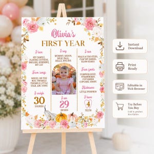May include: A white milestone birthday sign for Olivia's First Year featuring pink and white floral borders, gold text, and a central photograph of a baby. The sign lists categories including I love, I say, I can, Fave foods, and Fave songs.