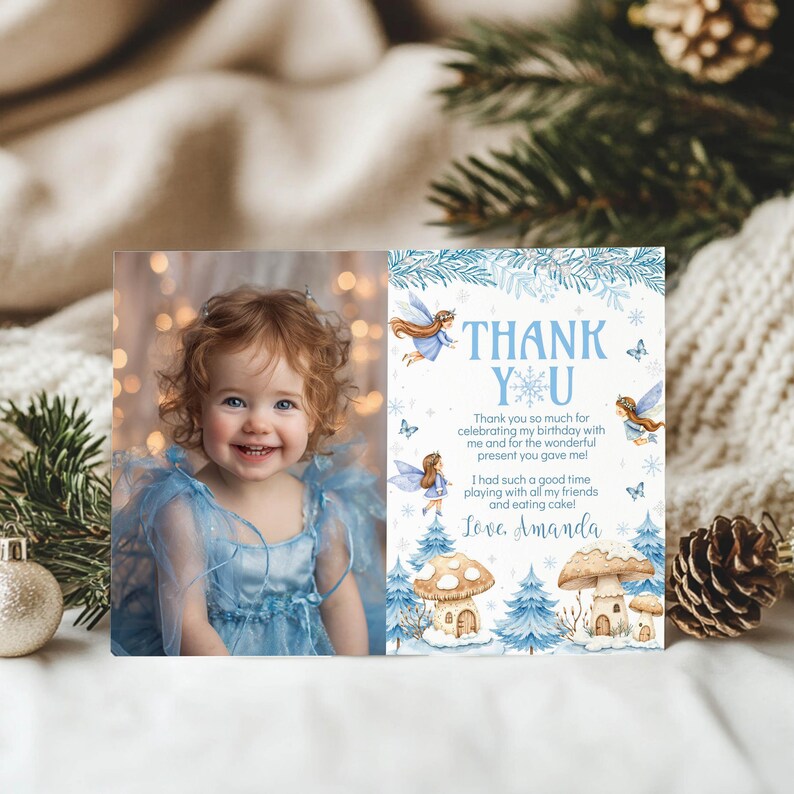 May include: A rectangular thank you card featuring a photo of a smiling child in a blue dress on the left and winter-themed illustrations of fairies, mushrooms, and blue pine trees on the right with the text Thank You and Love, Amanda.