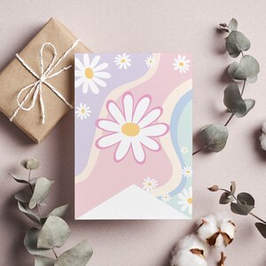 Op de afbeelding: Een rechthoekige wenskaart met een grafisch ontwerp van witte madeliefjes met gele harten tegen een achtergrond van golvende, pastelkleurige strepen in tinten lavendel, lichtroze en zachtblauw, met een wit driehoekig gedeelte aan de onderkant.