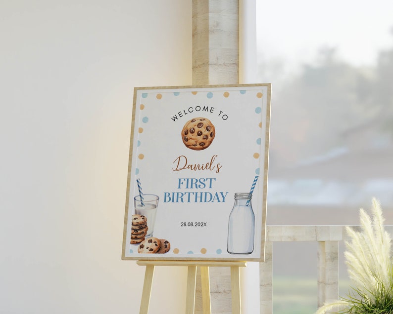 May include: Welcome to Daniel's First Birthday sign with a blue and brown polka dot background. The sign features a chocolate chip cookie, a glass of milk with a straw, and a bottle of milk. The date 28.08.202X is printed on the sign.