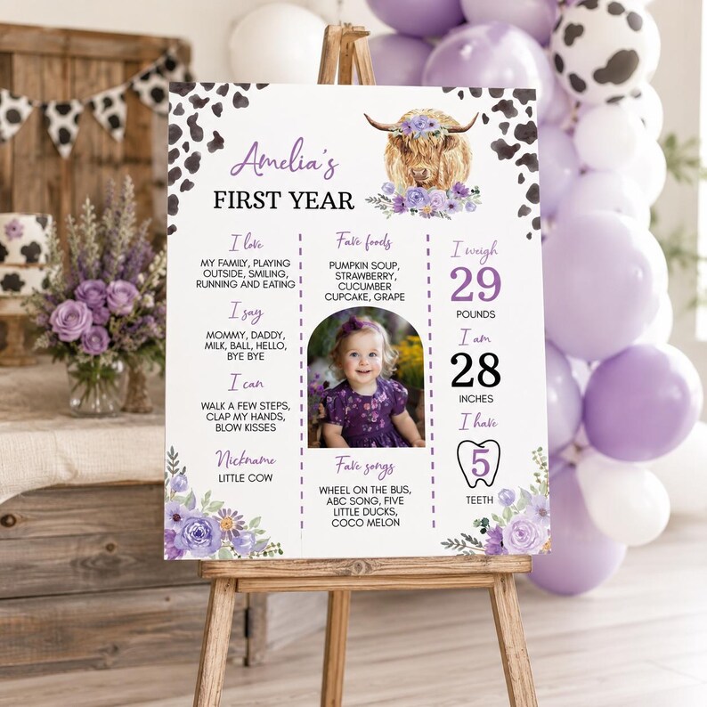May include: A white milestone birthday sign featuring a highland cow illustration with purple flowers, cow print borders, and text detailing Amelia's first year, including favorite foods, songs, 29 pounds, 28 inches, and 5 teeth.