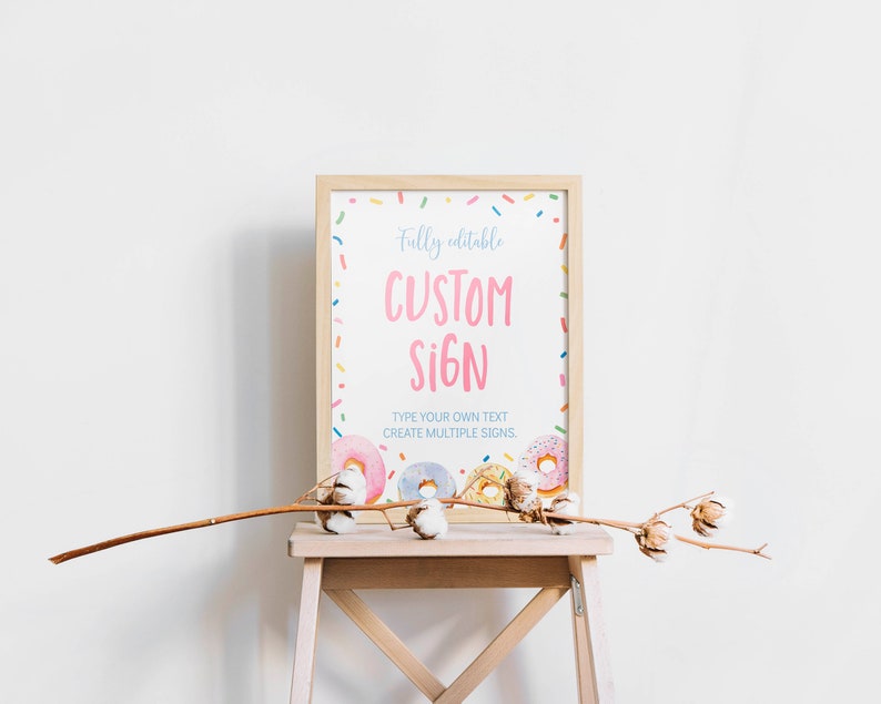 K&ouml;nnte beinhalten: Ein rechteckiges Schild in einem hellen Holzrahmen mit wei&szlig;em Hintergrund, bunten Streuseln, rosa, blauen und gelben Donuts sowie dem Text Fully editable CUSTOM SIGN, TYPE YOUR OWN TEXT, CREATE MULTIPLE SIGNS in Rosa und Blau.