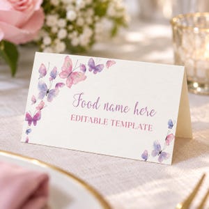 Peut inclure: Un marque-place en papier cartonn&eacute; blanc pli&eacute; orn&eacute; d'aquarelles de papillons dans des tons roses et violets. Le texte indique Food name here et EDITABLE TEMPLATE dans une police scripte et sans-serif violette, dispos&eacute; sur les bords.