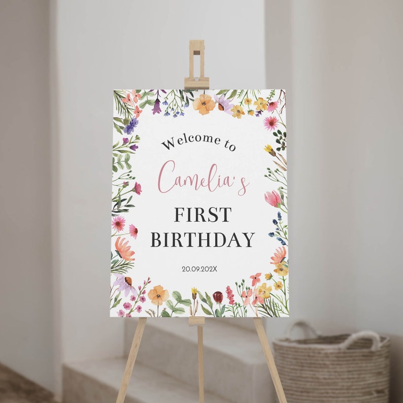 K&ouml;nnte beinhalten: Ein rechteckiges Schild auf einer Holzstaffelei mit einem Aquarell-Blumenrand aus rosa, gelben, orangen und violetten Wildblumen. Der Text lautet Welcome to Camelia's FIRST BIRTHDAY 20.09.202X in schwarzen und rosa Schriftarten.