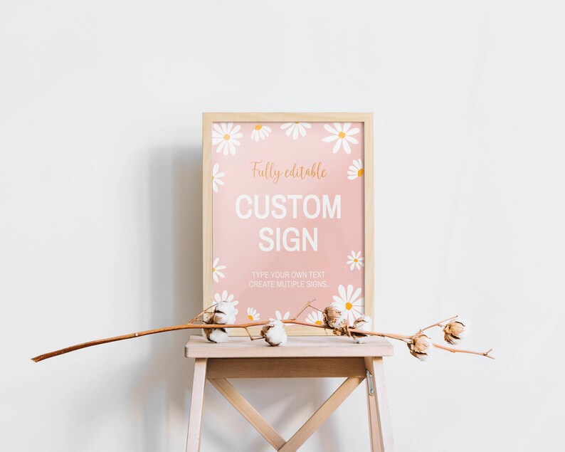 May include: A rectangular sign in a light wood frame featuring a pink background with white daisy illustrations. The text reads: Fully editable CUSTOM SIGN. TYPE YOUR OWN TEXT CREATE MUTIPLE SIGNS. A dried cotton branch rests in front of the frame.