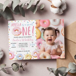 May include: A pink and white donut-themed first birthday invitation with a photo of a baby girl smiling. The invitation says "Amelia is a sweet one!" and includes details for the party, including the date, time, and location. RSVP information is also included.