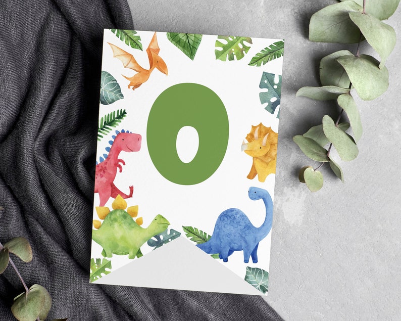K&ouml;nnte beinhalten: Ein wei&szlig;es, rechteckiges Wimpelf&auml;hnchen mit einem gro&szlig;en gr&uuml;nen Buchstaben O in der Mitte, umgeben von Aquarellillustrationen eines roten Dinosauriers, eines gelben Triceratops, eines blauen Langhalsdinosauriers, eines orangefarbenen Flugsauriers und gr&uuml;nen Bl&auml;ttern.