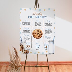 May include: A blue and brown first birthday milestone poster with a cookie theme. The poster includes details about the child's age, weight, height, favorite foods, toys, songs, and words. The poster is decorated with blue and brown polka dots.