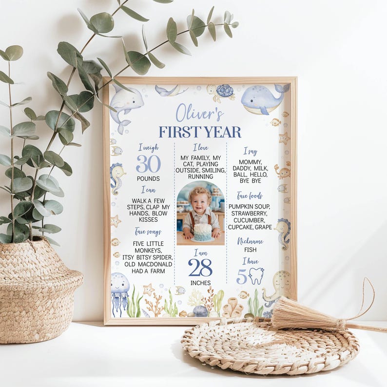 May include: A framed milestone poster titled Oliver's First Year, featuring blue sea creature illustrations, a central photo of a child with a cake, and text detailing weight of 30 pounds, height of 28 inches, favorite foods, songs, and nicknames.