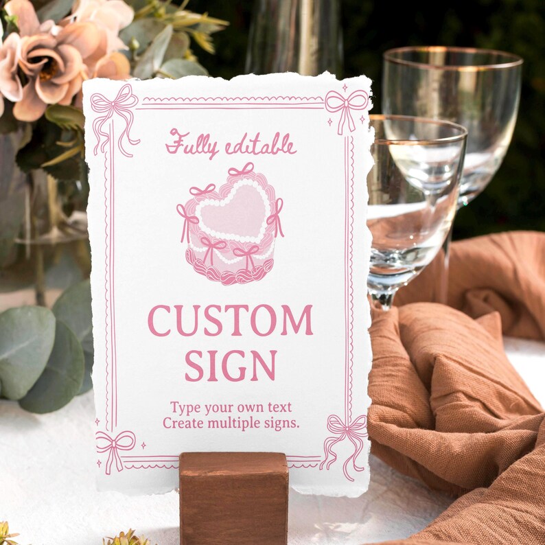 Peut inclure: Un panneau rectangulaire blanc aux bords d&eacute;chir&eacute;s, orn&eacute; d'un dessin au trait rose repr&eacute;sentant un g&acirc;teau en forme de c&oelig;ur avec des n&oelig;uds, une bordure d&eacute;corative et le texte "Fully editable", "CUSTOM SIGN" et "Type your own text Create multiple signs."