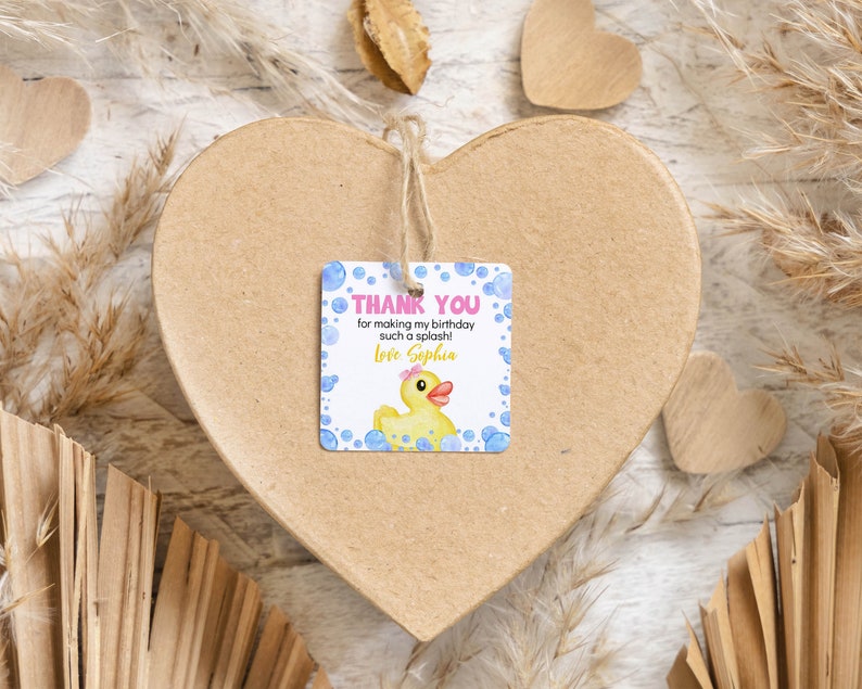 Pu&ograve; includere: Un'etichetta regalo quadrata in carta con una papera di gomma gialla con un fiocco rosa, bolle blu e il testo: THANK YOU for making my birthday such a splash! Love Sophia. L'etichetta &egrave; fissata con uno spago a una grande scatola di cartone a forma di cuore.