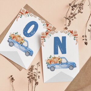 May include: Two white rectangular cards featuring a watercolour illustration of a blue vintage truck carrying orange pumpkins and autumn foliage. The left card displays the blue letter O, and the right card displays the blue letter N in a bold font.