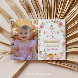 May include: A rectangular thank you card featuring a photo of a baby in a pink dress on the left and text on the right. The text reads: THANK YOU, Thank you so much for celebrating my birthday with me and for the wonderful present you gave me! I had such a good time playing with all my friends and eating cake! Love, Olivia. The right side is decorated with a watercolour floral and pumpkin wreath.