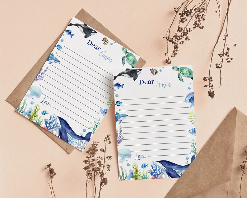 Pu&ograve; includere: Due fogli di carta da lettere bianchi con righe orizzontali, decorati con illustrazioni ad acquerello di creature marine tra cui una balena, uno squalo, una tartaruga e una medusa. Il testo "Dear Huson" e "Love" &egrave; stampato in blu, con buste marroni.